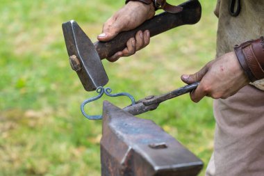 Demirci elinde çekiçle bir örsün üzerinde demiri şekillendiriyor.