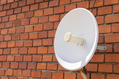 Kahverengi duvarın önündeki beyaz çanak anten.