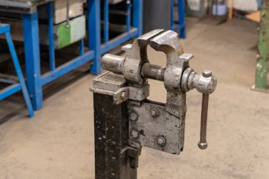 Eski, yıpranmış, gri boyalı bir mengene boş bir kaynakçının ortasında.