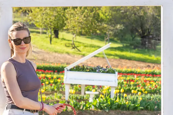 Beyaz piyanolu ve lale bahçeli güneş gözlüklü sarışın kadın.