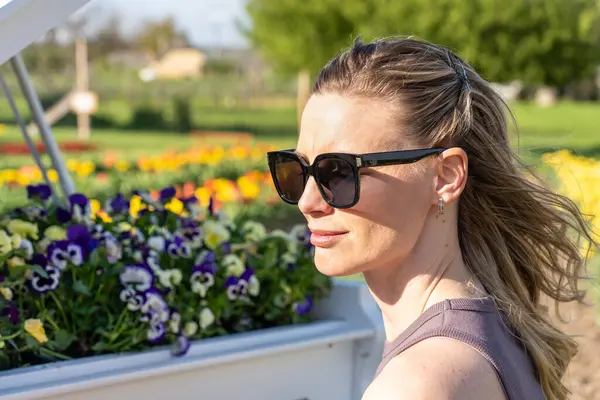 Arkasında bahar sarısı laleleri olan beyaz piyanonun başındaki sarışın kadın.