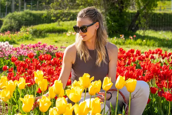 Güneş gözlüklü genç sarışın kadın renkli lale tarlasında oturuyor.