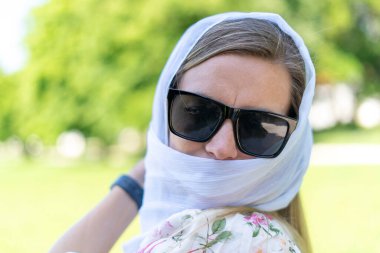 Güneş gözlüklü, açık havada beyaz atkısı olan zarif sarışın kadın.