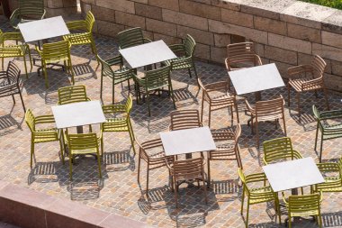 Açık kafe terasında renkli boş masalar ve sandalyeler var.