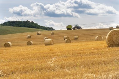 Macaristan 'da bir yamaçta yaz güneşinde saman balyaları ve arka planda bir traktör..