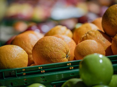 Bir markette veya markette yeşil plastik bir sandıkta portakalların ve yeşil elmaların yakın çekim görüntüsü. Ön plan bulanık arkaplanlı narenciye meyvesinin dokulu yüzeyine odaklanır..