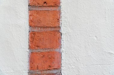 İki büyük alçı yüzeyin arasına gömülü tek bir dikey kırmızı tuğla şeridi. Görüntü, pürüzsüz alçı ve pürüzsüz tuğla arasındaki dokunsal kontrastı yakalıyor ve ince bir görsel gerilim uyandırıyor. Kompozisyon son derece minimalistik ve... 