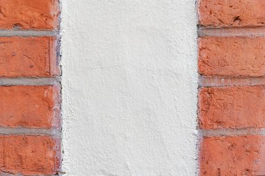 Her iki taraftaki kırmızı tuğlalarla çerçevelenmiş ortada beyaz bir alçı parçası. Fotoğraf, tuğlanın kaba dokusu ile daha pürüzsüz alçı yüzey arasındaki geçişi ve etkileşimi yakalıyor. Yayılmış doğal ışıkla kafa kafaya alınan görüntü,