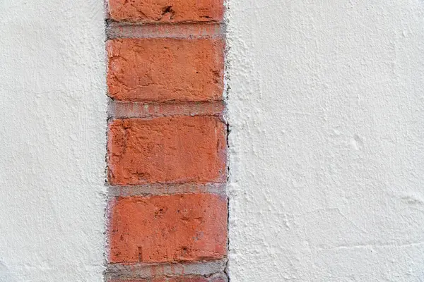 İki büyük alçı yüzeyin arasına gömülü tek bir dikey kırmızı tuğla şeridi. Görüntü, pürüzsüz alçı ve pürüzsüz tuğla arasındaki dokunsal kontrastı yakalıyor ve ince bir görsel gerilim uyandırıyor. Kompozisyon son derece minimalistik ve... 