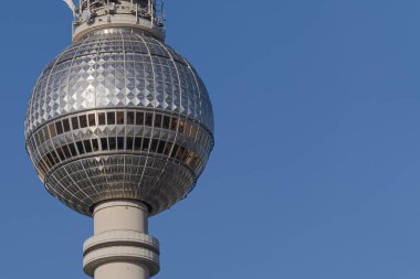 Berlin TV Kulesi 'nin (Fernsehturm) yatay görüntüsü, metalik kürenin alt kısmını ve beton destek sütunun tepesini parlak mavi gökyüzüne karşı gösteriyor..