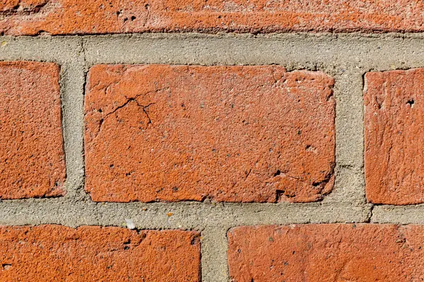 Görünür çatlakları ve pürüzlü dokusu olan tuğla duvardaki kırmızı bir tuğlaya yakın plan..