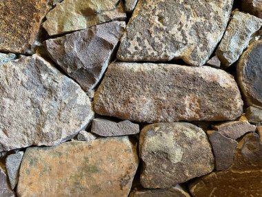 Close-up and detailed view of a natural stone wall displaying its organic textures and patterns, characterized by rough-edged stones of different shapes and sizes, in earthy tones. clipart