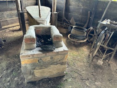 Kırsal, antika bir demirci atölyesinin içinde örs, demir ocağı ve aletlerle. Bu ayar, eski ahşap kirişler ve toprak dokularla geçmişin işçiliğine geri dönüşünü yansıtıyor..