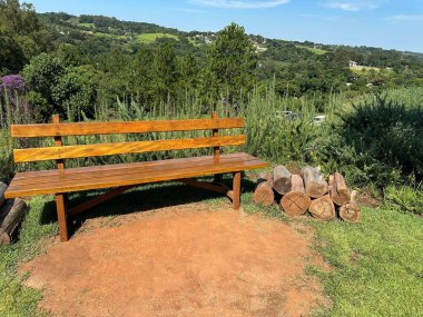 A serene park setting with a wooden bench with a pile of firewood on a sunny day, surrounded by lush green trees and expansive landscape. Ideal for relaxation and enjoying nature. clipart