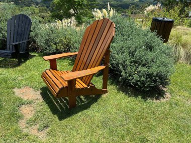 Davetkar ahşap bir Adirondack sandalyesi, canlı çalılar ve doğal manzaralarla çevrili yemyeşil bir çimenlikte oturur ve sakin bir açık hava rahatlama noktasının özünü yakalar..