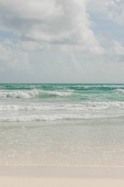 Tulum, Quintana Roo, Meksika 'da bulutlu bir günde kumsal beyaz kuma çarpan dalgalar dışında bomboştur. Su, cam gibi berrak bir turkuazdır ve tüm sahne cennet gibi görünür..
