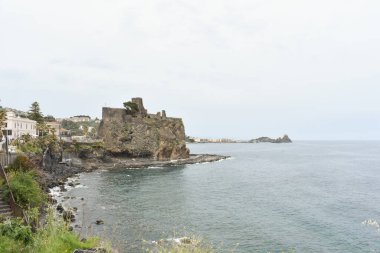 Aci Castello Sicilya 'daki Norman eski ortaçağ Şatosu Akdeniz kıyısında kaya duvarları ve bulutlu bir günde arka planda Aci Trezza, Güney İtalya, Catania.