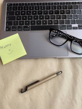 İş yeri. Çevrimiçi eğitim kavramı. E-öğrenme. Online eğitim. Dizüstü bilgisayar, kalem ve gözlük, üst görüş, fotokopi alanı, afiş. Modern çalışma ortamı. El yazısıyla yazılmış mutlu bir not.. 