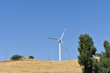 İtalya, Sicilya 'daki dağda rüzgar türbini. Rüzgar türbini ve kırsal İtalyan yaz manzarası. Mountain Eolic Parkı. Yenilenebilir enerji kavramı, yeşil ekolojik enerji üretimi. 