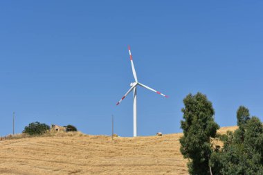 İtalya, Sicilya 'daki dağda rüzgar türbini. Rüzgar türbini ve kırsal İtalyan yaz manzarası. Mountain Eolic Parkı. Yenilenebilir enerji kavramı, yeşil ekolojik enerji üretimi. 