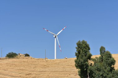 İtalya, Sicilya 'daki dağda rüzgar türbini. Rüzgar türbini ve kırsal İtalyan yaz manzarası. Mountain Eolic Parkı. Yenilenebilir enerji kavramı, yeşil ekolojik enerji üretimi. 