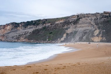 Arkasında engebeli uçurumlar ve kıyı boyunca hafif dalgalar olan engin altın plajlar. Doğa, seyahat ve kıyı manzarası projeleri için ideal.