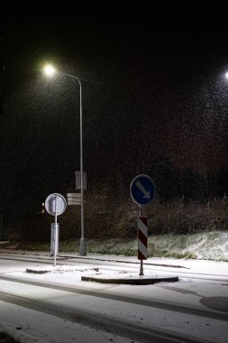 Gece sakin, karlı bir kavşak, parlayan sokak lambaları ve trafik ışıklarıyla aydınlanan, kentsel bir ortamda kışın dinginliğini yakalayan. Mevsimlik ve şehir temaları için mükemmel