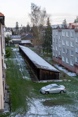 Hafif karla kaplı çimenli bir alan, park edilmiş bir araba ve bir apartman bloğunun yanında depolama binaları bulunan şehir konutları. Kış, banliyö ve mimari temalar için ideal.