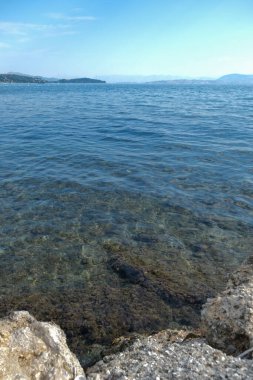 Kristal berraklığında deniz suyu kayalık bir kıyı şeridini nazikçe suyla kaplayarak sualtı dokularını ortaya çıkarır ve sakin bir sahil manzarası oluşturur. Deniz kenarında huzurlu bir an.