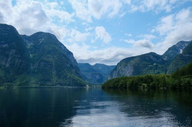 Derin mavi gölü olan ve yemyeşil tepeleri ve parlak gökyüzünü yansıtan bir dağ vadisini nefes kesen bir manzara. Görüntü, el değmemiş doğa, seyahat, macera ve manzara temaları için mükemmel.