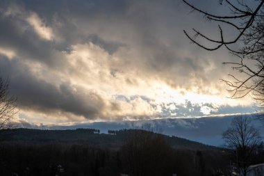 Orman tepelerinde güneş ışığı alan kara bulutlar. Manzara dramatik havayı ve karamsar atmosferi yakalıyor..