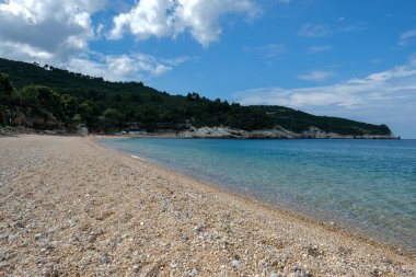 Turkuaz denizi ve arka planda ormanlı tepeleri olan terk edilmiş eğimli bir sahil.