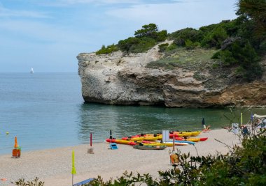 Sakin bir sahilde renkli kanolar ve arka planda kayalık bir uçurum.