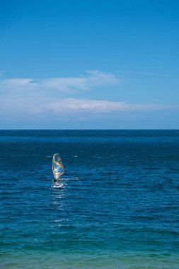 Rüzgâr sörfçüsü açık gökyüzünün altında kayalık kıyılarda süzülüyor