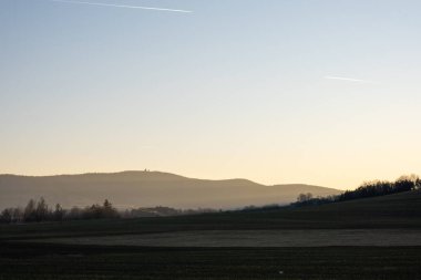 Kırsal tepelerin ve tarlaların üzerinde sabah sisi yumuşak gün doğumu ışığı, ufuktaki uzak dağlar