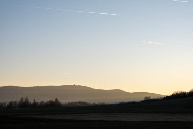 Kırsal tepelerin ve tarlaların üzerinde sabah sisi yumuşak gün doğumu ışığı, ufuktaki uzak dağlar