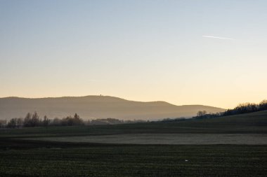 Kırsal tepelerin ve tarlaların üzerinde sabah sisi yumuşak gün doğumu ışığı, ufuktaki uzak dağlar