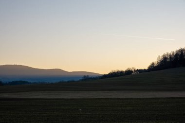 Uzak tepeler ve sabah sisi katmanları olan tarım arazileri gün doğumunda, manzara üzerindeki yumuşak sıcak ışık