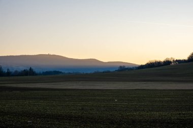 Uzak tepeler ve sabah sisi katmanları olan tarım arazileri gün doğumunda, manzara üzerindeki yumuşak sıcak ışık