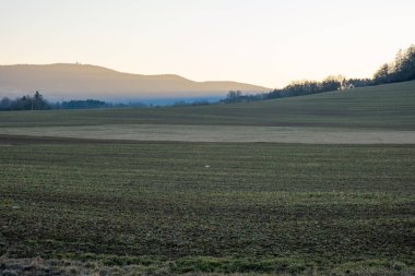 Uzak tepeler ve sabah sisi katmanları olan tarım arazileri gün doğumunda, manzara üzerindeki yumuşak sıcak ışık
