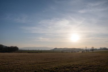 Elektrik hatları sisli tarlalar ve yumuşak gündoğumu ışığı altında uzak tepeler boyunca uzanan kırsal alan..