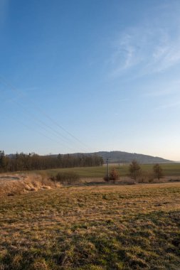 Elektrik direkleri ve kabloları kırsal alanda akşam ışığında tepeler boyunca uzanıyor.