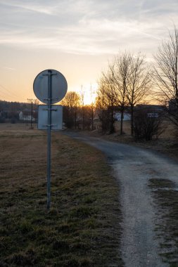 Dar kırsal yolda gün batımında trafik işaretinin arka görüntüsü, göz hizasında.