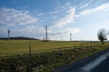 Elektrik direkleri çimenli kırsal alanlara yayılıyor mavi gökyüzünün altında baharda bulutlar
