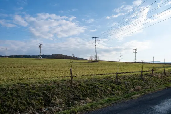 Elektrik direkleri çimenli kırsal alanlara yayılıyor mavi gökyüzünün altında baharda bulutlar