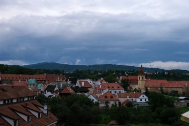 Dramatik fırtına bulutları altında kırmızı çatıları ve uzak tepeleri olan geleneksel Çek kasabasının panoramik manzarası.