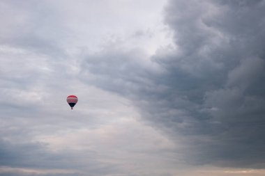 Gökyüzünde tek bir sıcak hava balonu havada süzülüyor ve arka planda dramatik bir doku oluşturuyor..