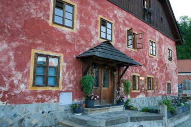 Kırsal, kırmızı boyalı, ahşap çerçeveli pencereli, taş basamaklı ve Avrupa 'da saksı çiçekli bir evin ön görüntüsü..