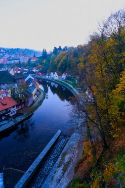 Sonbaharda Cesky Krumlov 'un kırmızı çatılı, şelaleli ve Vltava Nehri' ndeki evlerinin en üst manzarası. Canlı ağaçlar ve tarihi binalar.