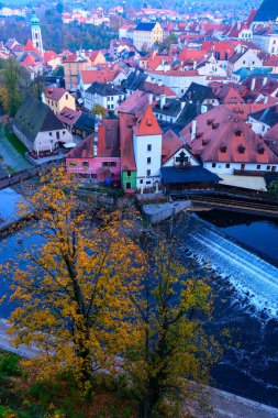 Sonbaharda kırmızı çatıları, şelalesi ve Vltava nehri olan Çek Krumlov evlerinin en iyi manzarası. Canlı ağaçlar ve tarihi binalar.